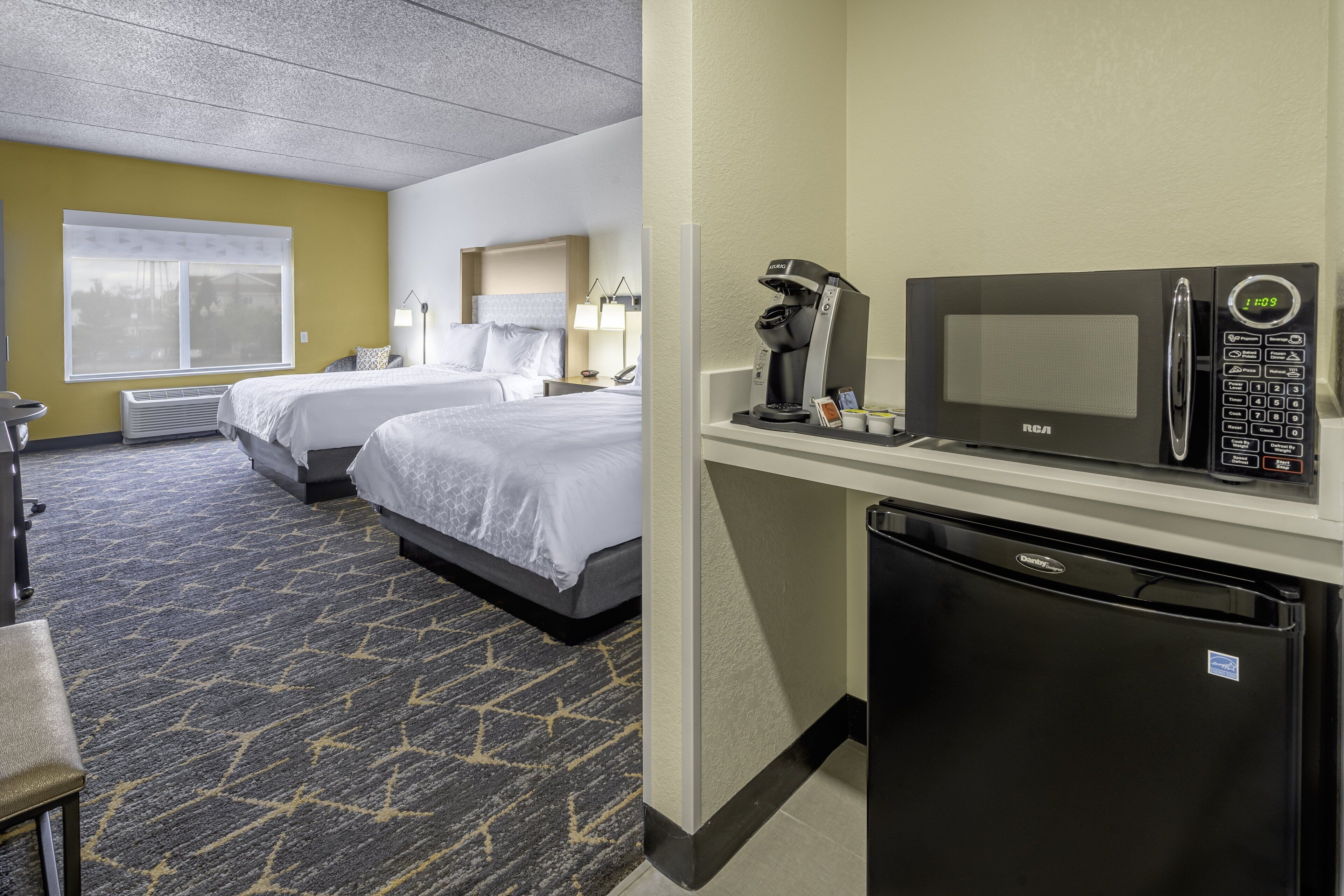 Une chambre d’hôtel avec deux lits, un minibar, une machine à café et un réfrigérateur.