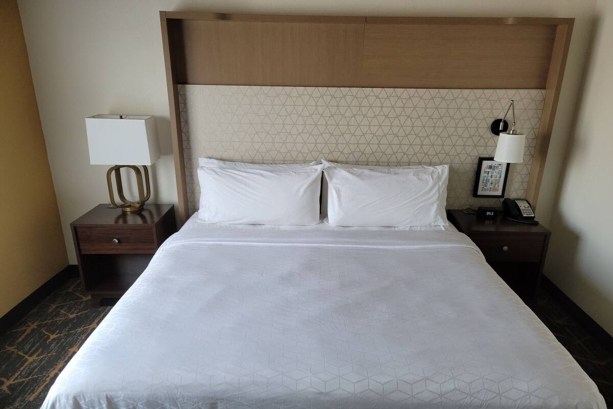 A hotel room with a large bed, two bedside tables, a nightstand, a lamp, a phone, and a framed picture on the wall.