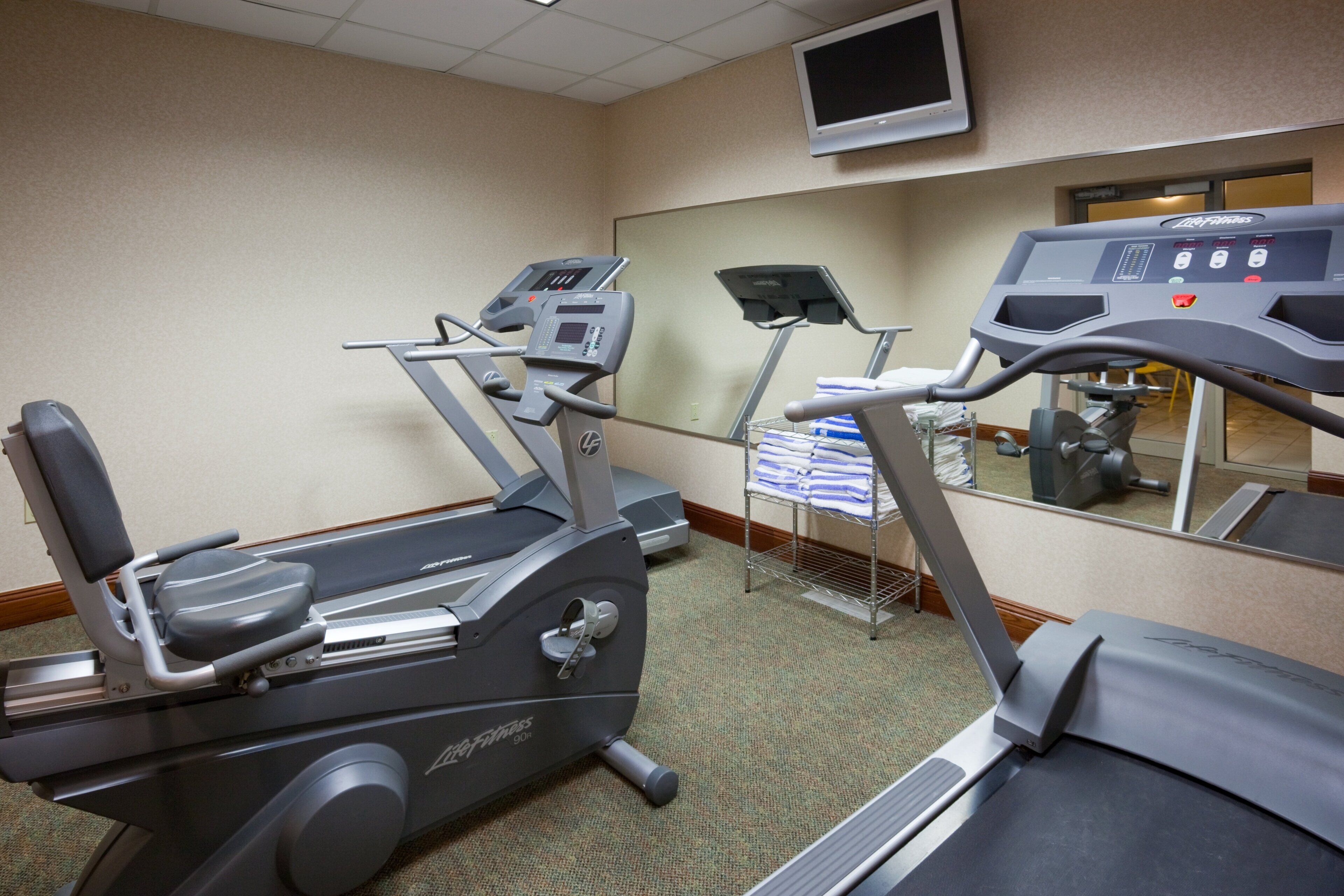 A fitness room with treadmills and a mirrored wall.