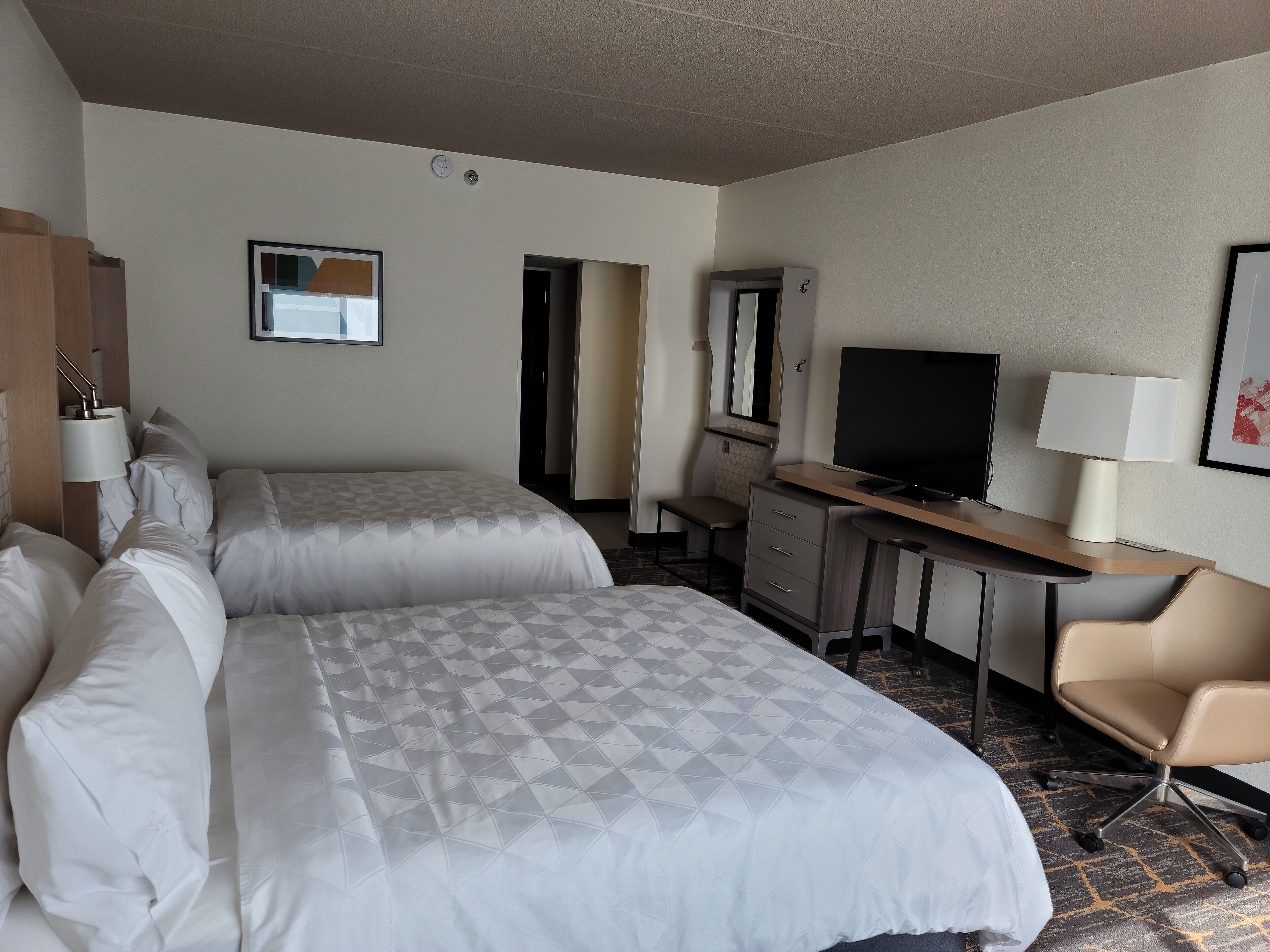 A hotel room with two beds, a desk with a TV, a chair, and a dresser.