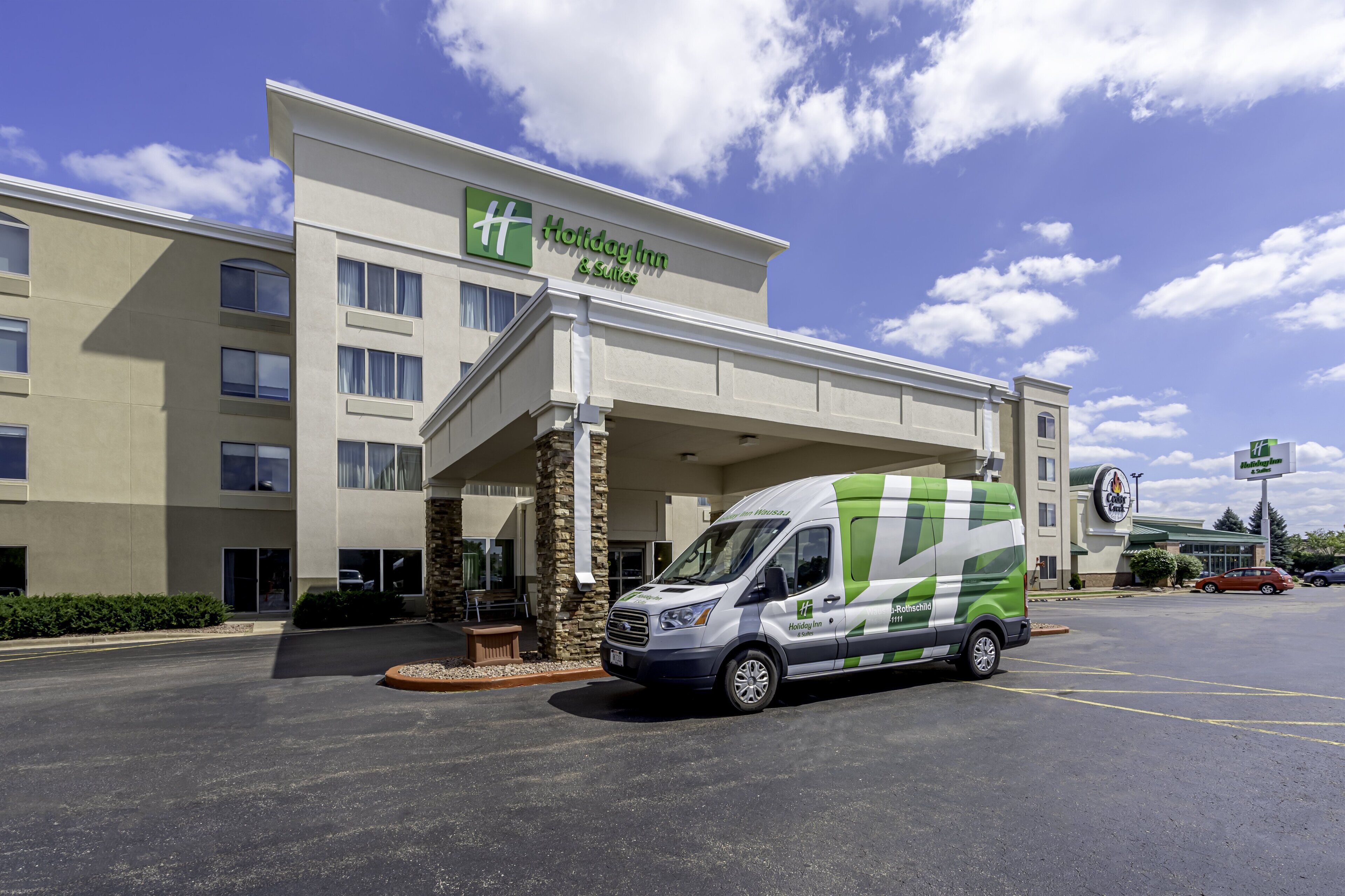 A Holiday Inn & Suites building with a parking lot and a green and white van in front.