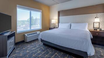A hotel room with a bed, a television, a desk, a lamp, and a window with a view of the outdoors.