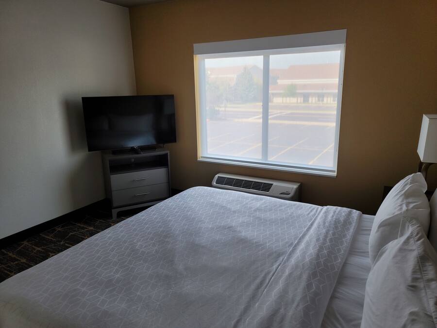 Una habitación de hotel con una cama, un televisor sobre una cómoda, una ventana con vistas a un estacionamiento y un calentador de pared.