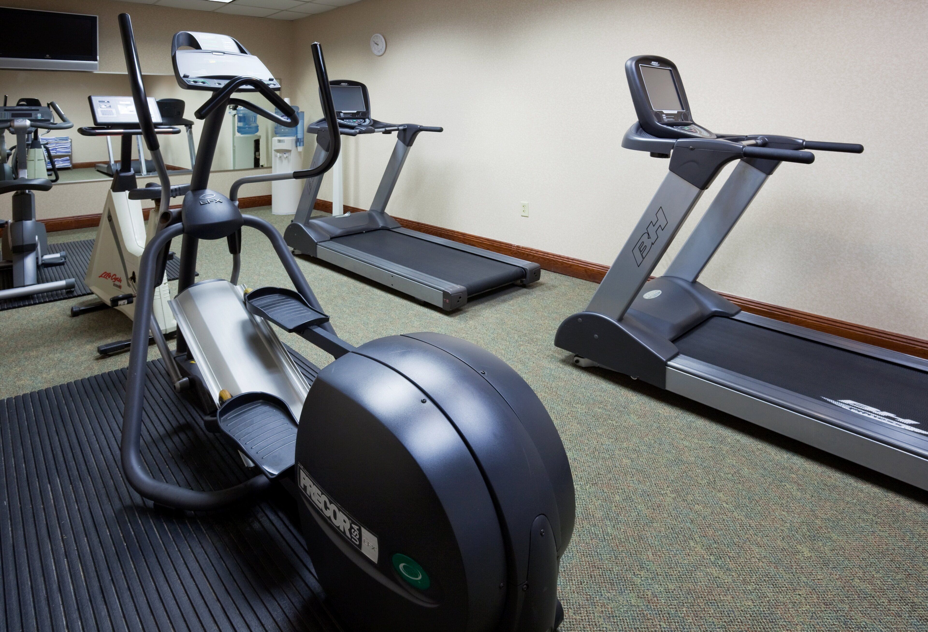 Un gimnasio con cintas de correr, elípticas y una bicicleta estática.