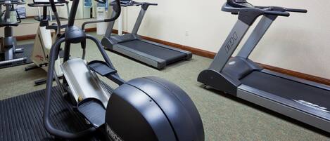 Un gimnasio con cintas de correr, elípticas y una bicicleta estática.