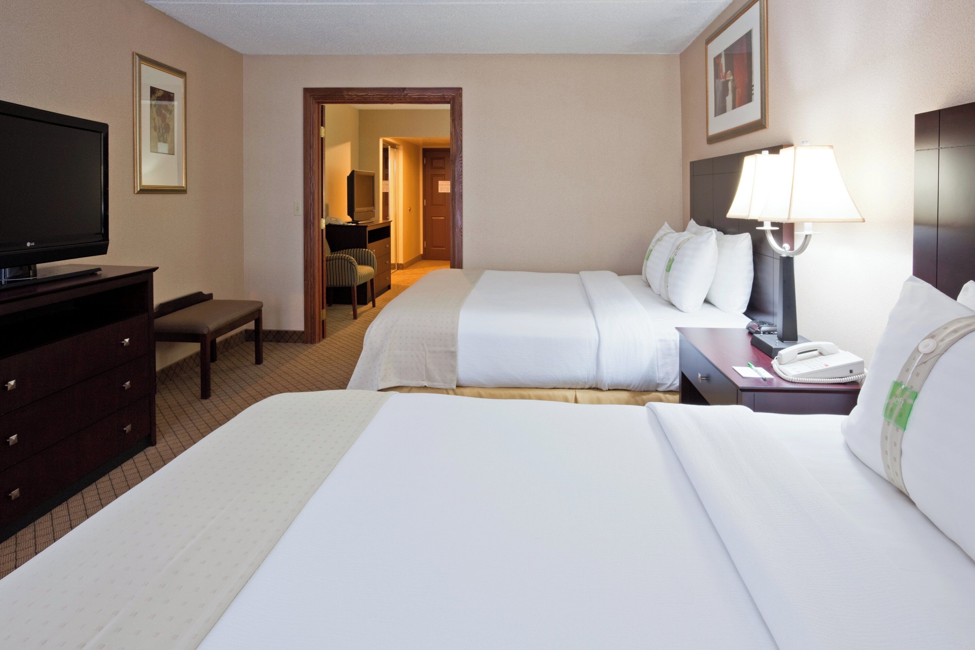 A hotel room with two beds, a television, a desk with a lamp, and a chair.