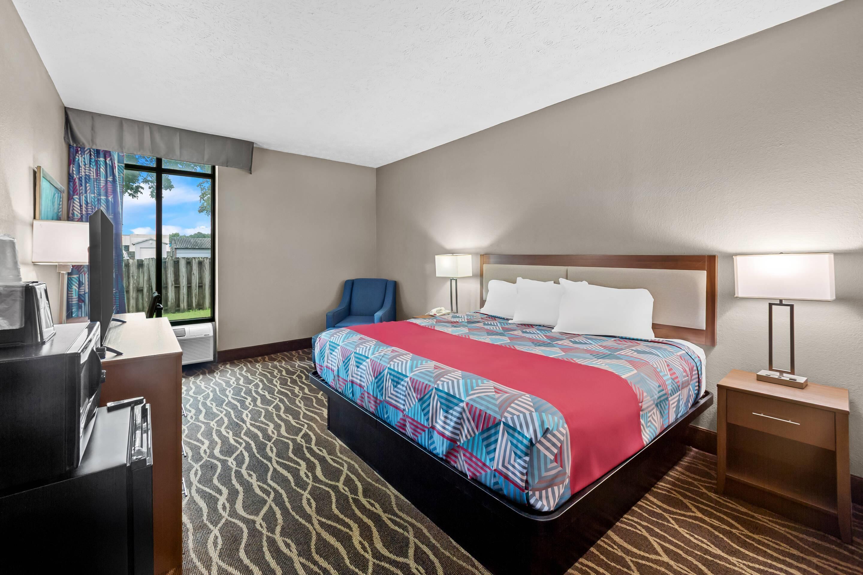 Una habitación de hotel con cama, escritorio, silla y mesita de noche.