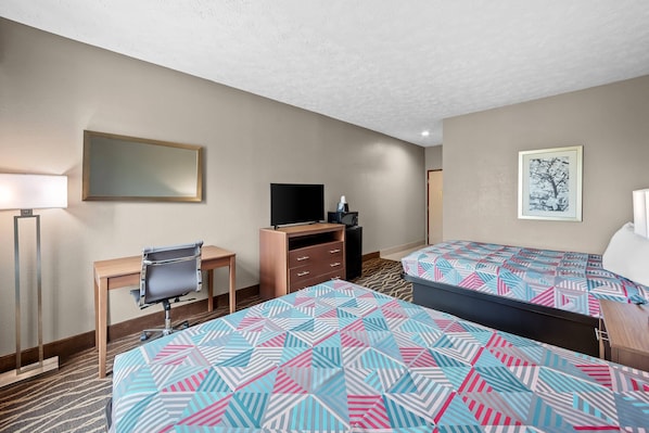 A hotel room with two beds, a desk, a chair, a TV, a dresser, and a framed picture on the wall.