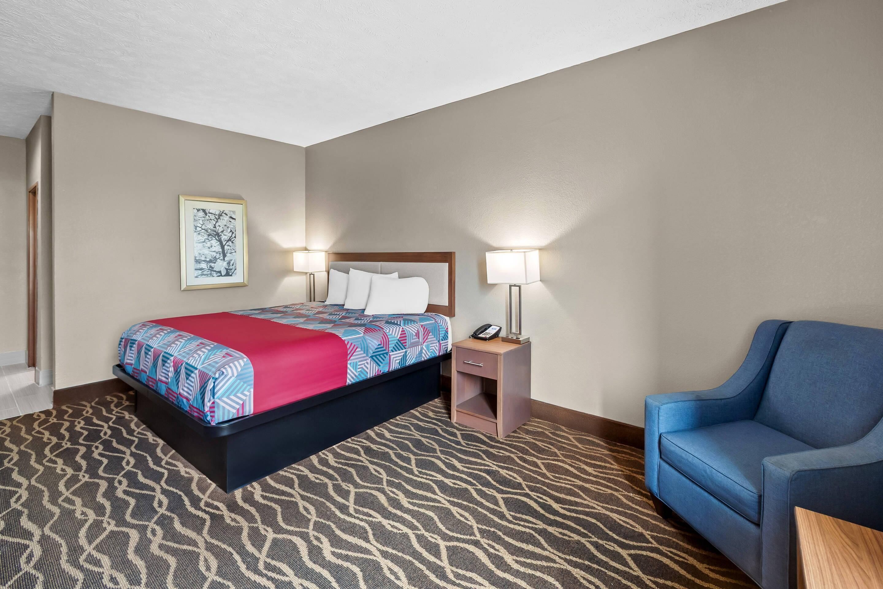 Una habitación de hotel con cama, mesitas de noche, una silla y piso alfombrado.