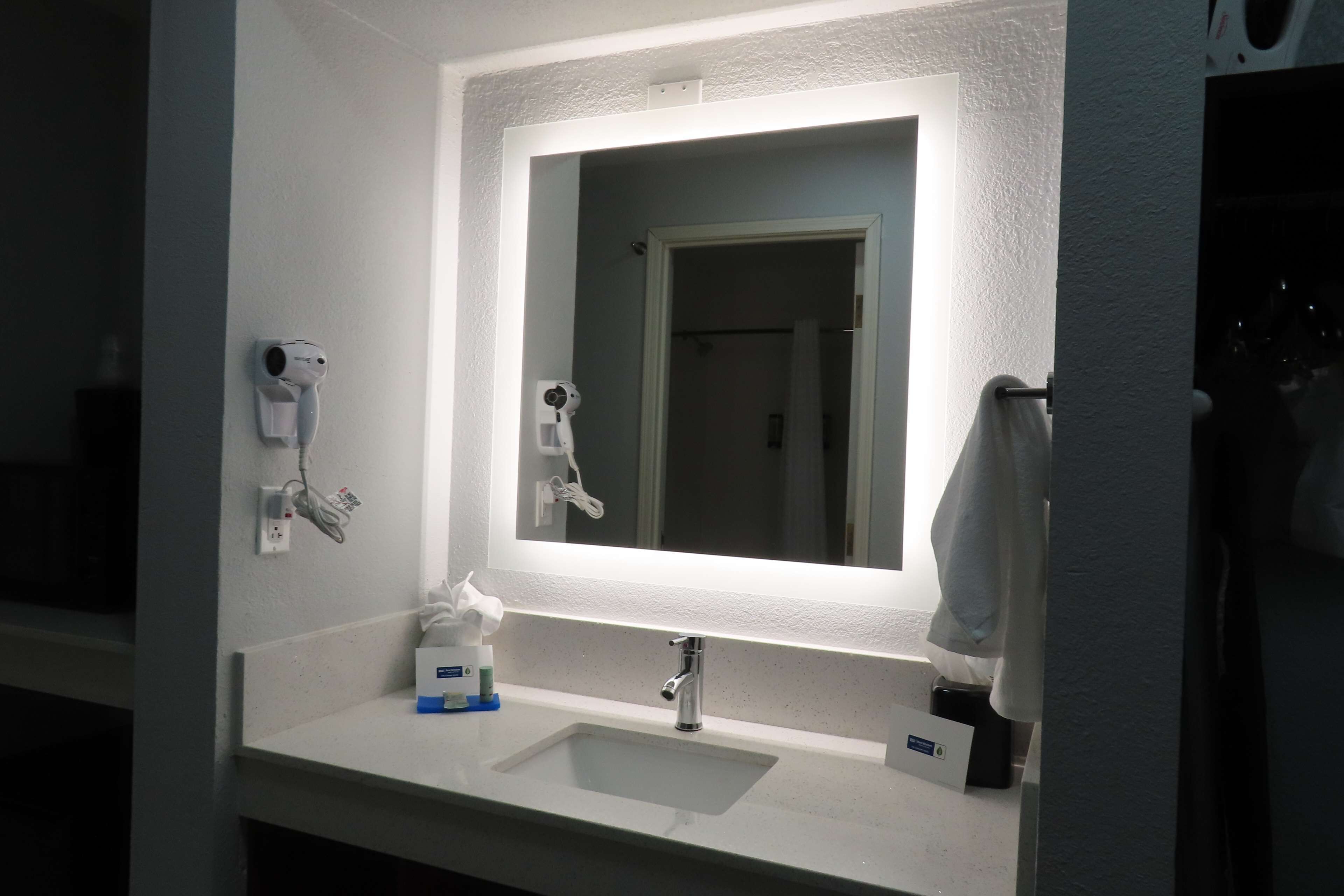 Une salle de bain avec un lavabo blanc, un miroir et un sèche-cheveux fixé au mur.