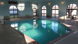 An indoor swimming pool with clear blue water, surrounded by arched windows and a tiled floor.