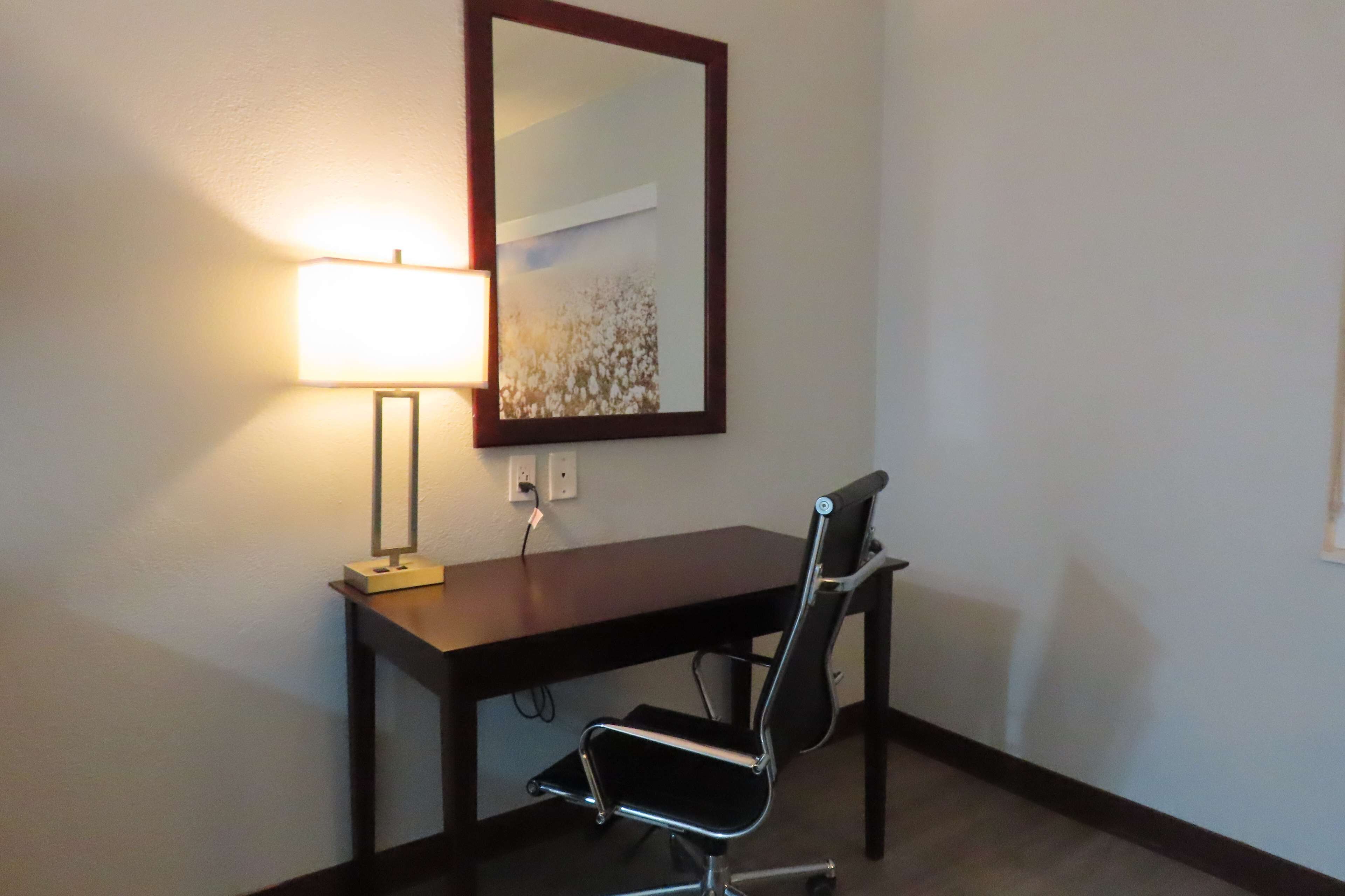 Un escritorio con una silla, una lámpara y un espejo en la pared.