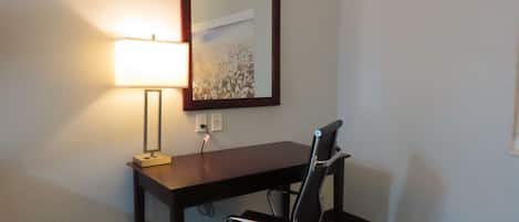 Un escritorio con una silla, una lámpara y un espejo en la pared.