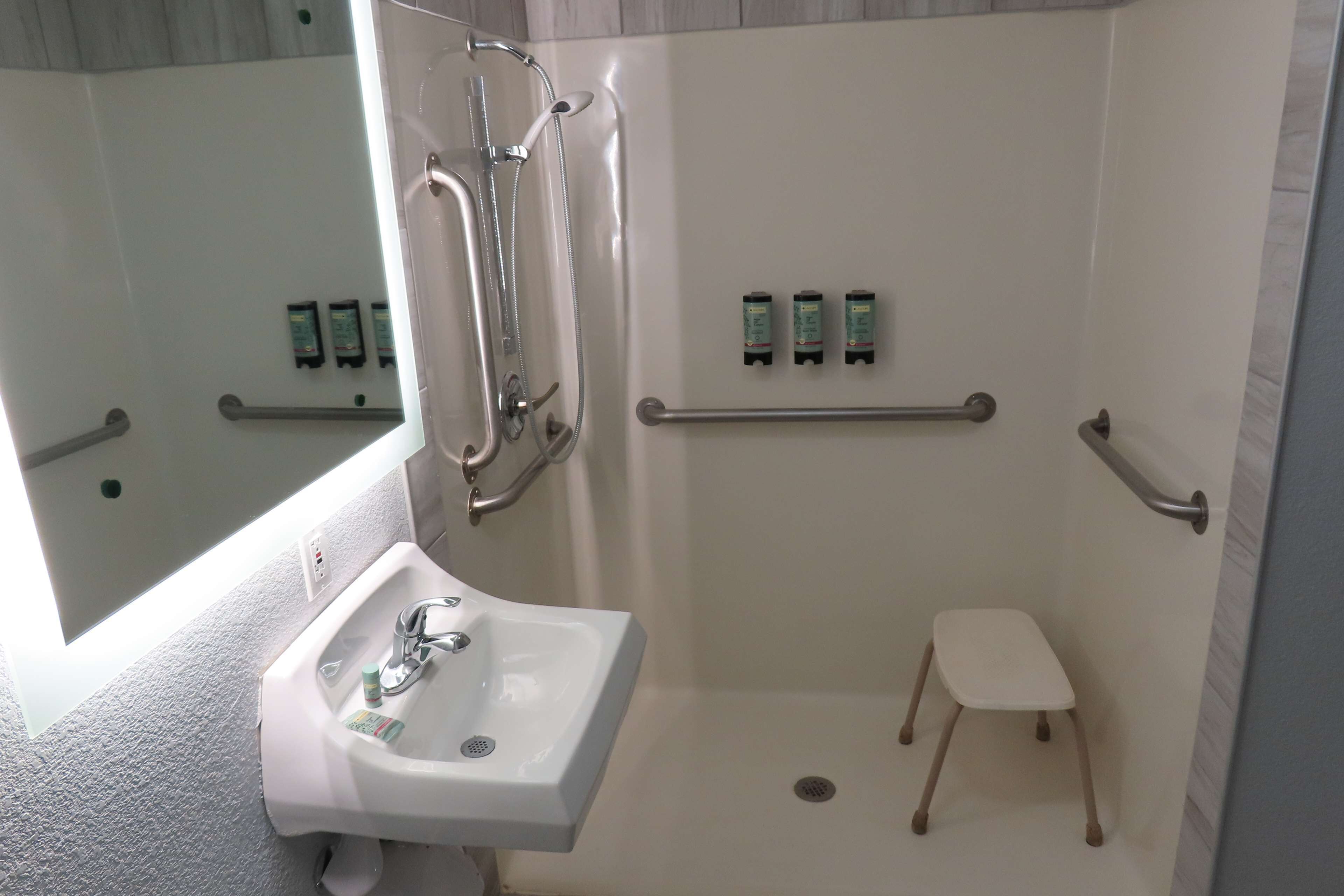 Une salle de bain moderne avec une douche à l’italienne, des barres d’appui, un lavabo et un petit tabouret.