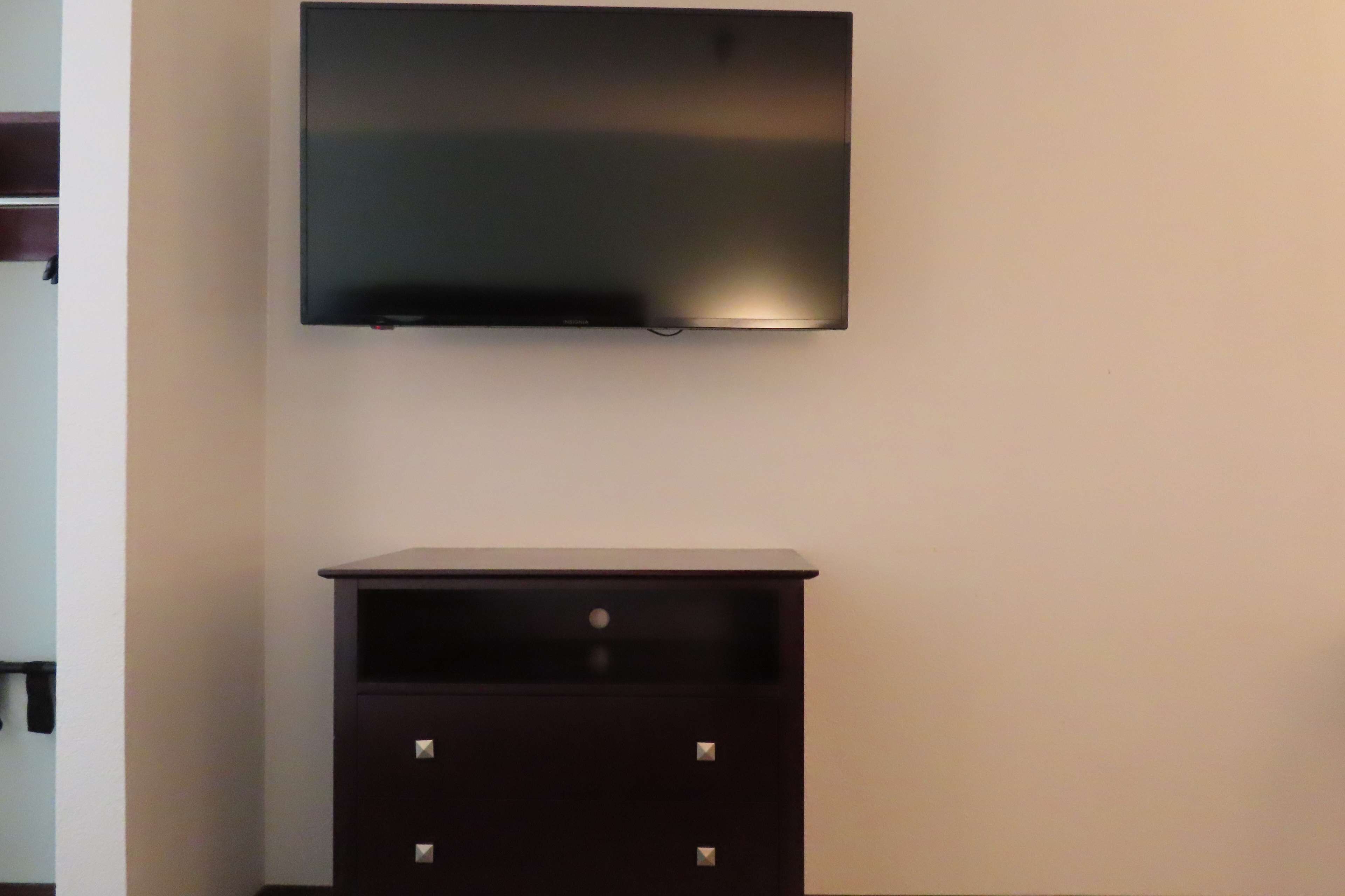 A flat-screen TV mounted on a wall above a dark wooden cabinet with two drawers.