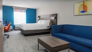 A hotel room with a bed, a blue sofa, a wooden coffee table, a desk with a chair, and a window with blinds. - Holiday Inn Express & Suites Kimball by IHG (South Pittsburg)
