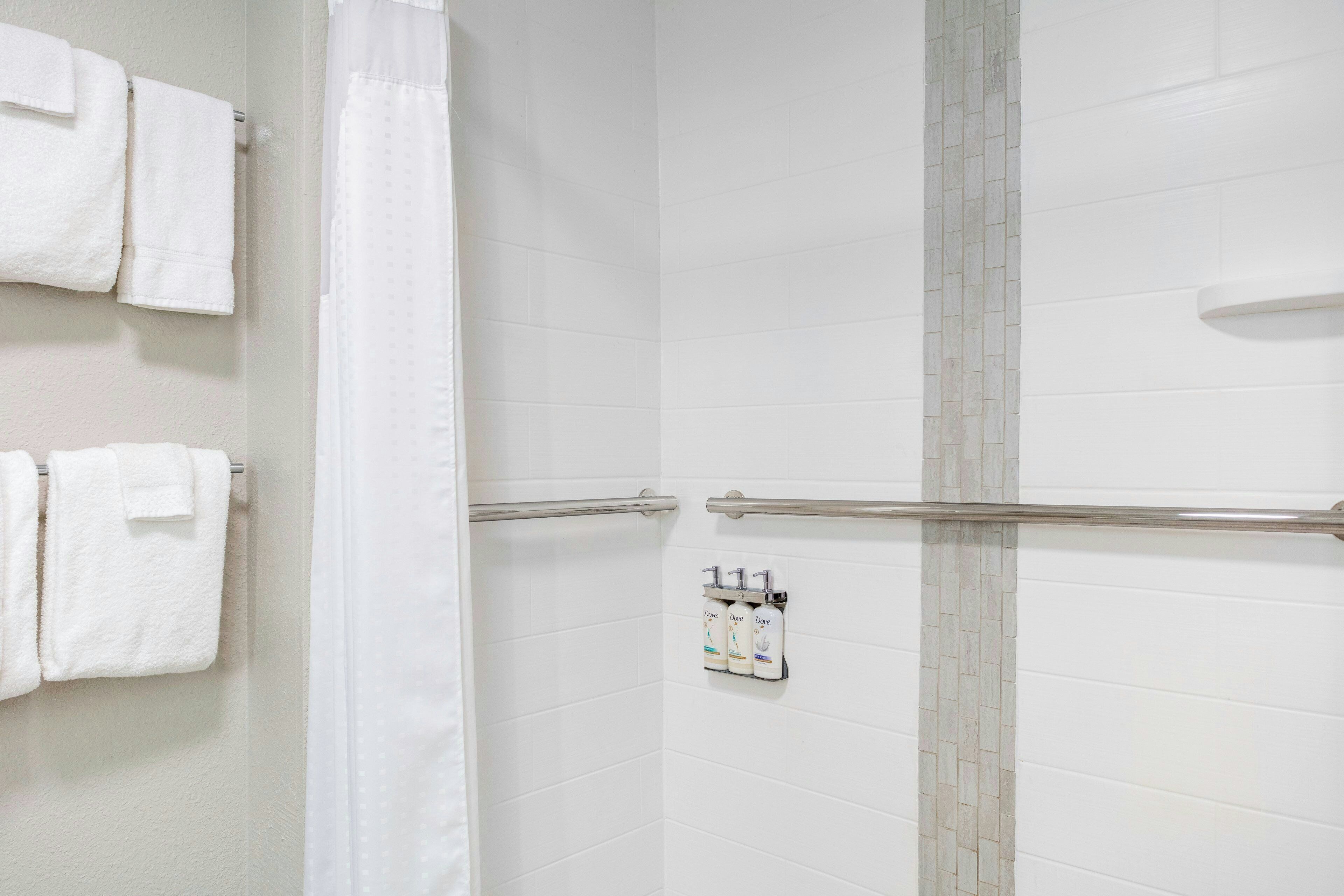 A bathroom with white tiled walls, a shower area, and a towel rack with folded towels.