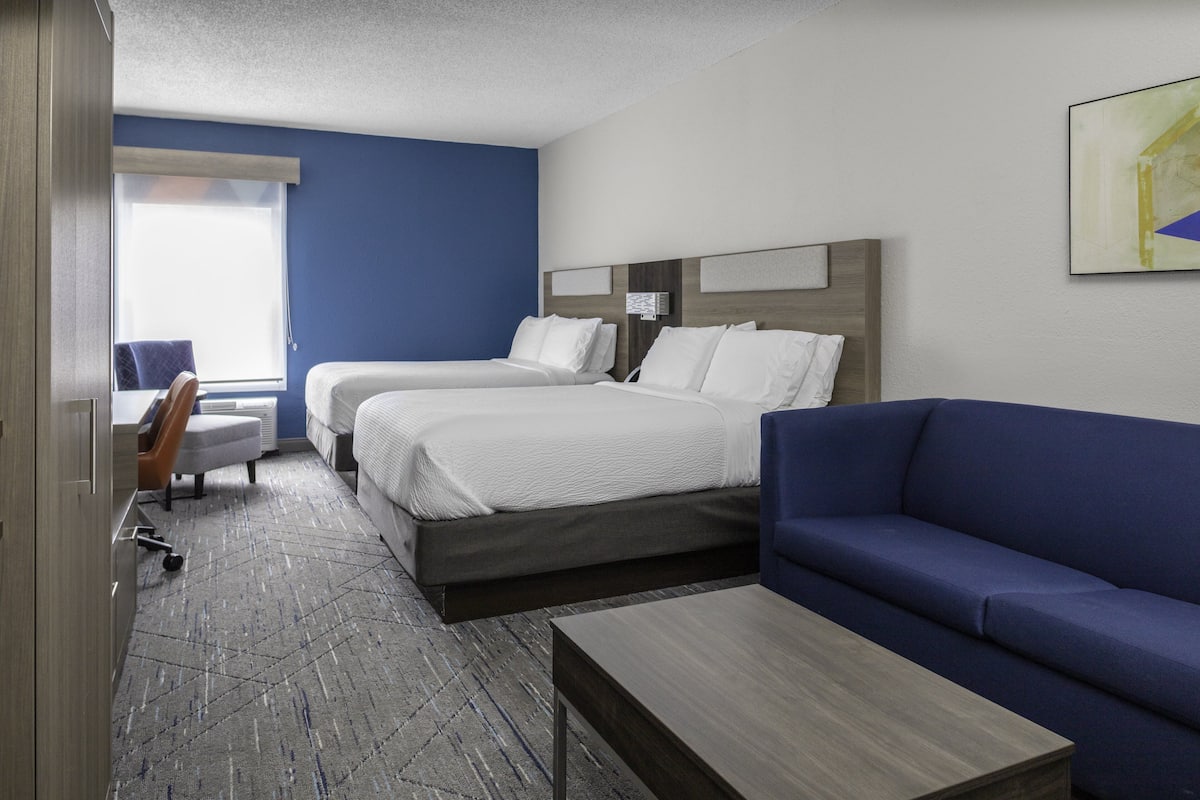 A hotel room with two beds, a sofa, a desk, and a chair.