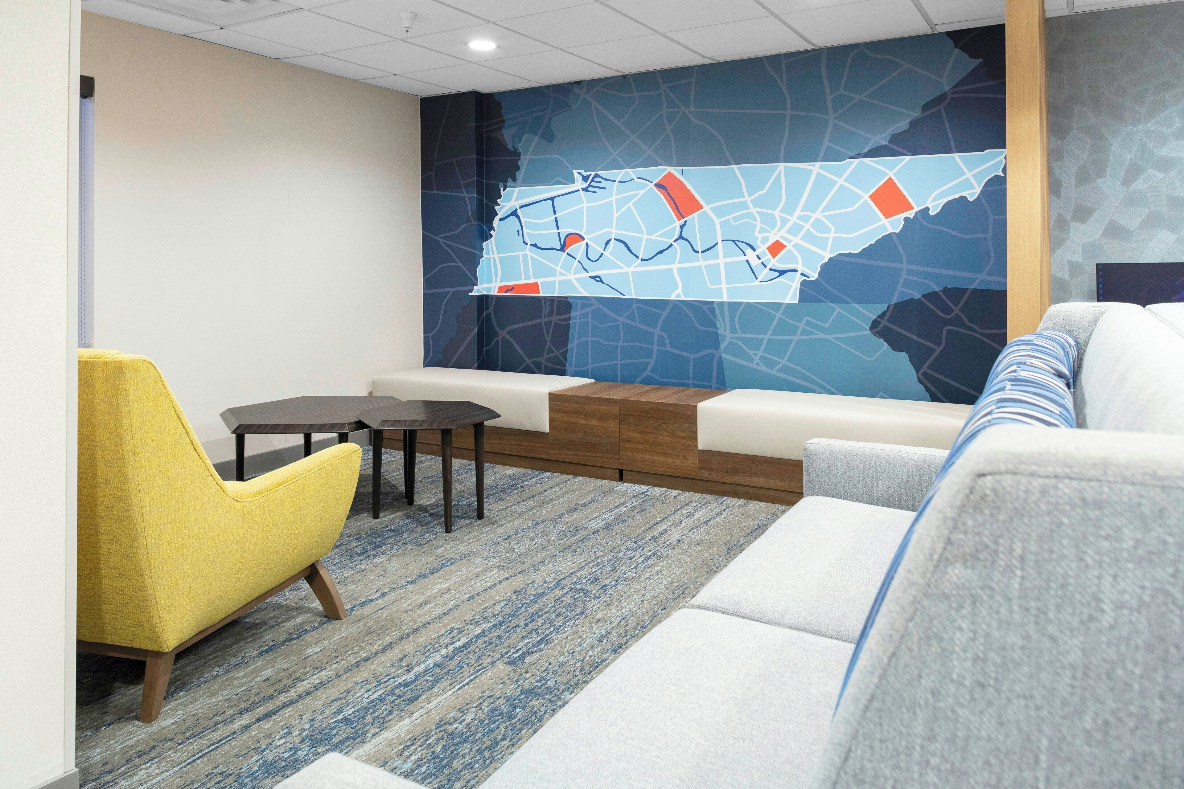 A modern office space with a sectional sofa, a yellow armchair, a small table, and a large wall map.
