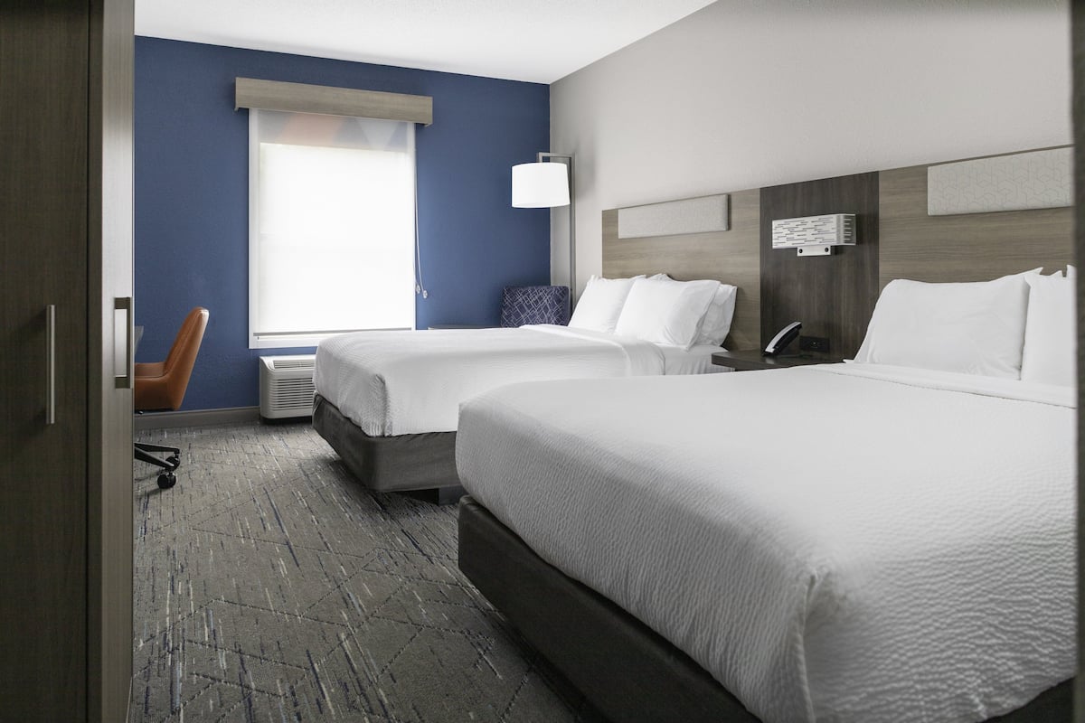 A hotel room with two beds, a desk, a chair, and a window with blinds.