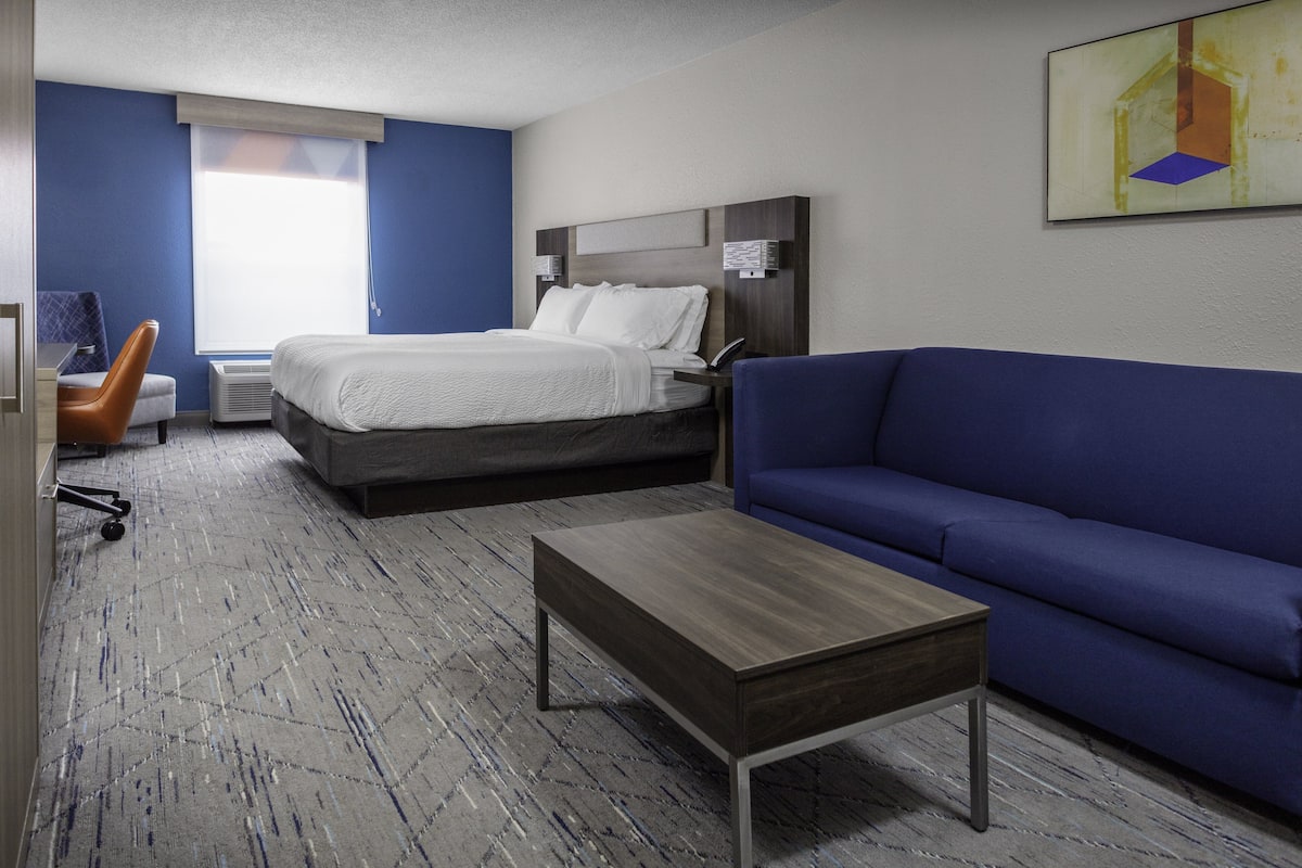 A hotel room with a bed, a blue sofa, a wooden coffee table, and a desk with a chair.