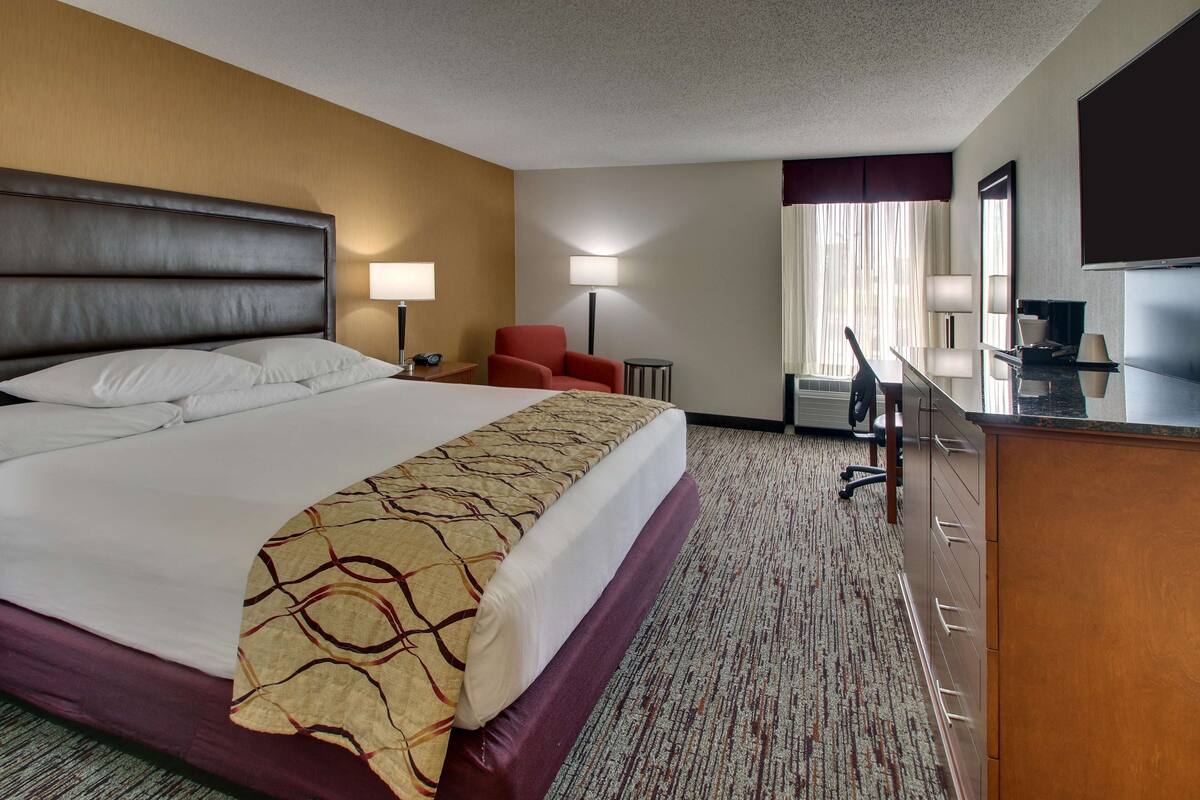 A hotel room with a large bed, a desk, a chair, a TV, and a window with curtains.