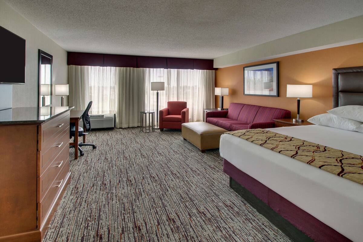 A hotel room with a bed, a desk, a chair, a sofa, and a TV.