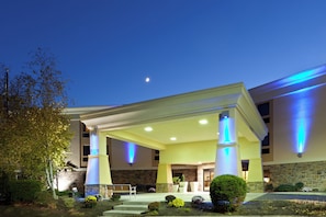 Un hotel con entrada cubierta, fachada de piedra y columnas iluminadas.