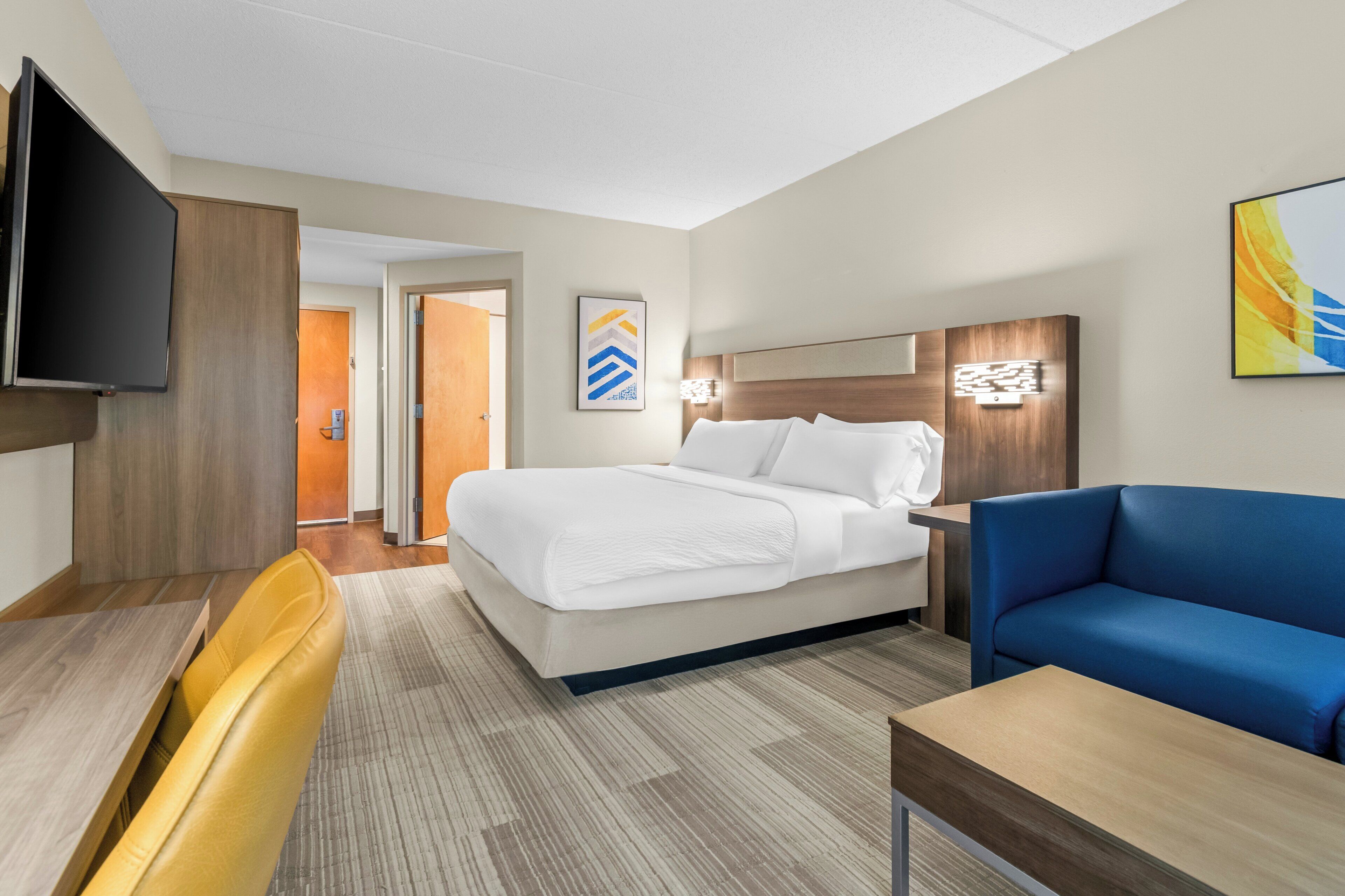 Een hotelkamer met een bed, een slaapbank, een televisie, een bureau en een deur naar een andere kamer.