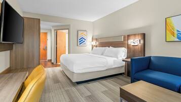Een hotelkamer met een bed, een slaapbank, een televisie, een bureau en een deur naar een andere kamer.