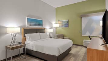 A hotel room with a bed, two bedside tables with lamps, a desk with a television, and artwork on the walls.