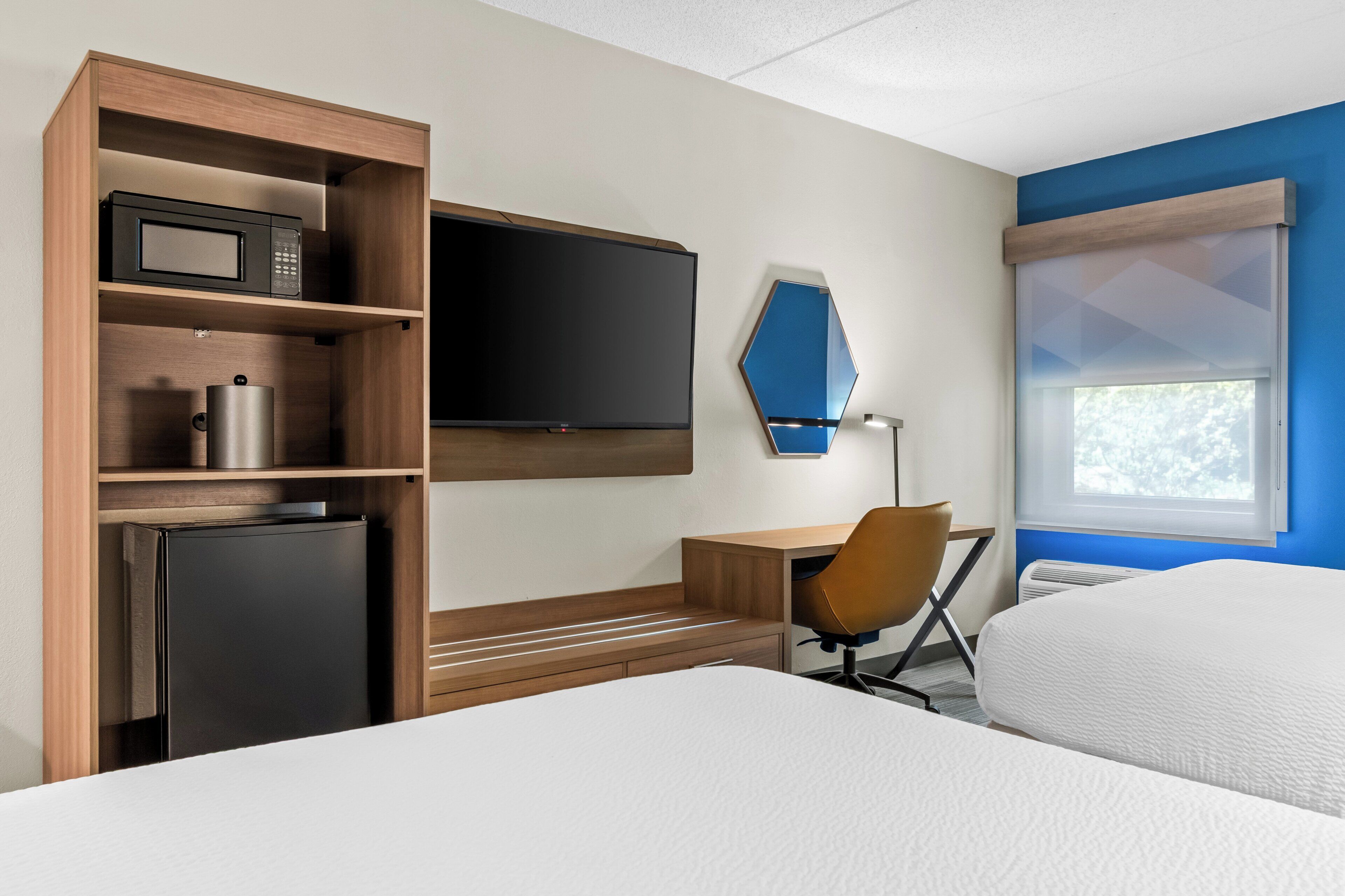Habitación de hotel con cama, escritorio, silla, televisor, microondas y refrigerador.