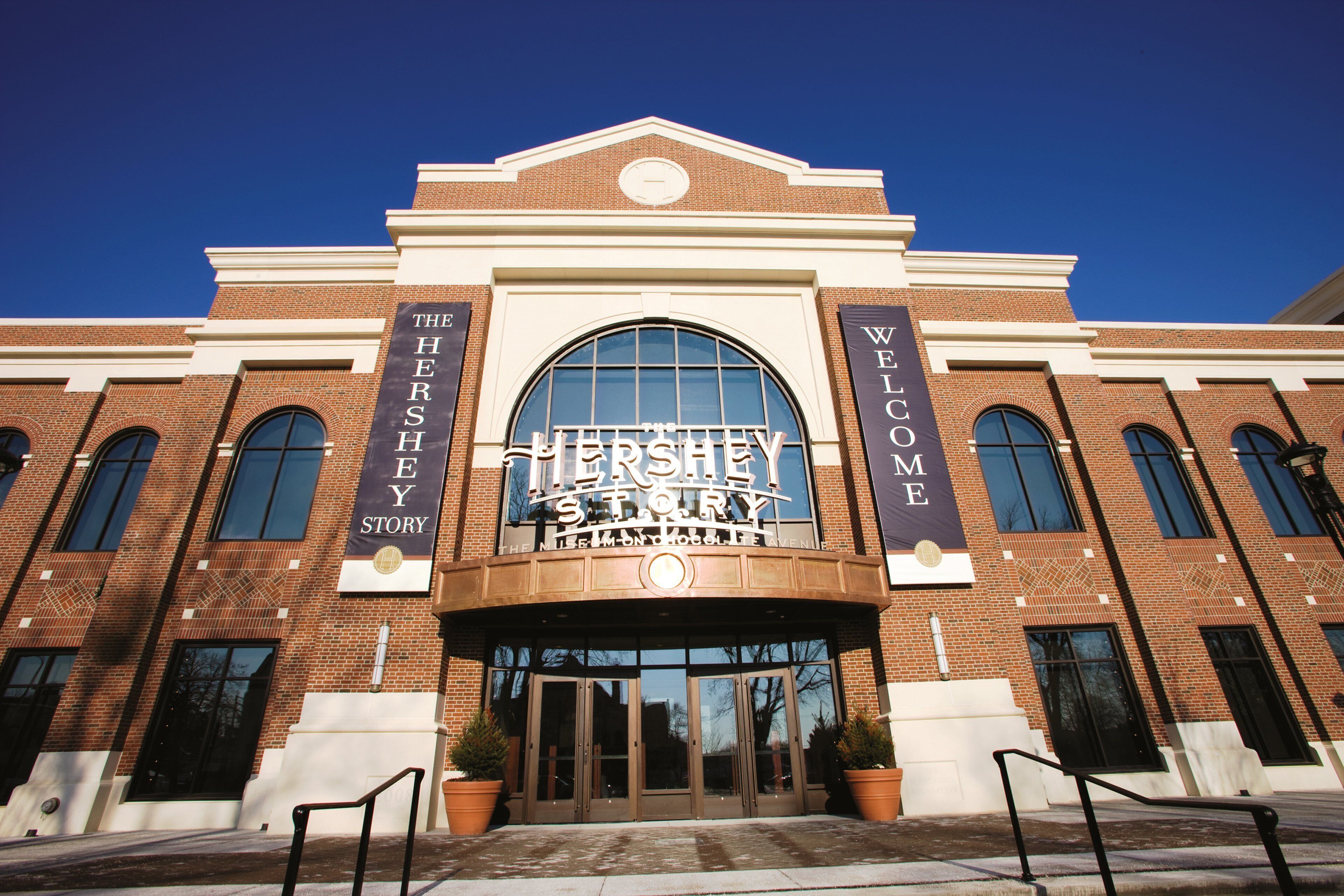 A Hershey's Story Museum with a large arched entrance, brick facade, and two banners on either side.