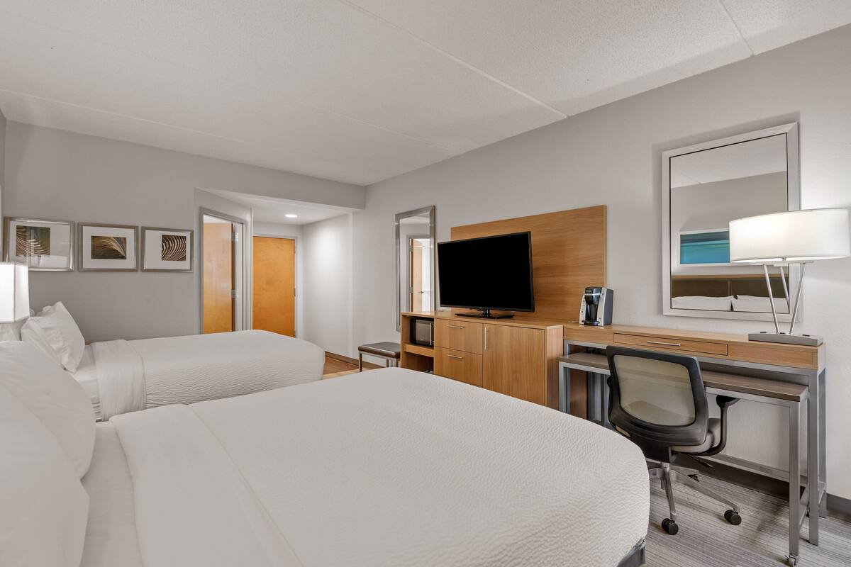 A hotel room with two beds, a desk with a chair, a TV, and a mirror.