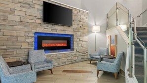 A modern living room with a stone wall, a flat-screen TV, a fireplace, and two armchairs. - Holiday Inn Express Hershey - Harrisburg Area by IHG (Hummelstown)