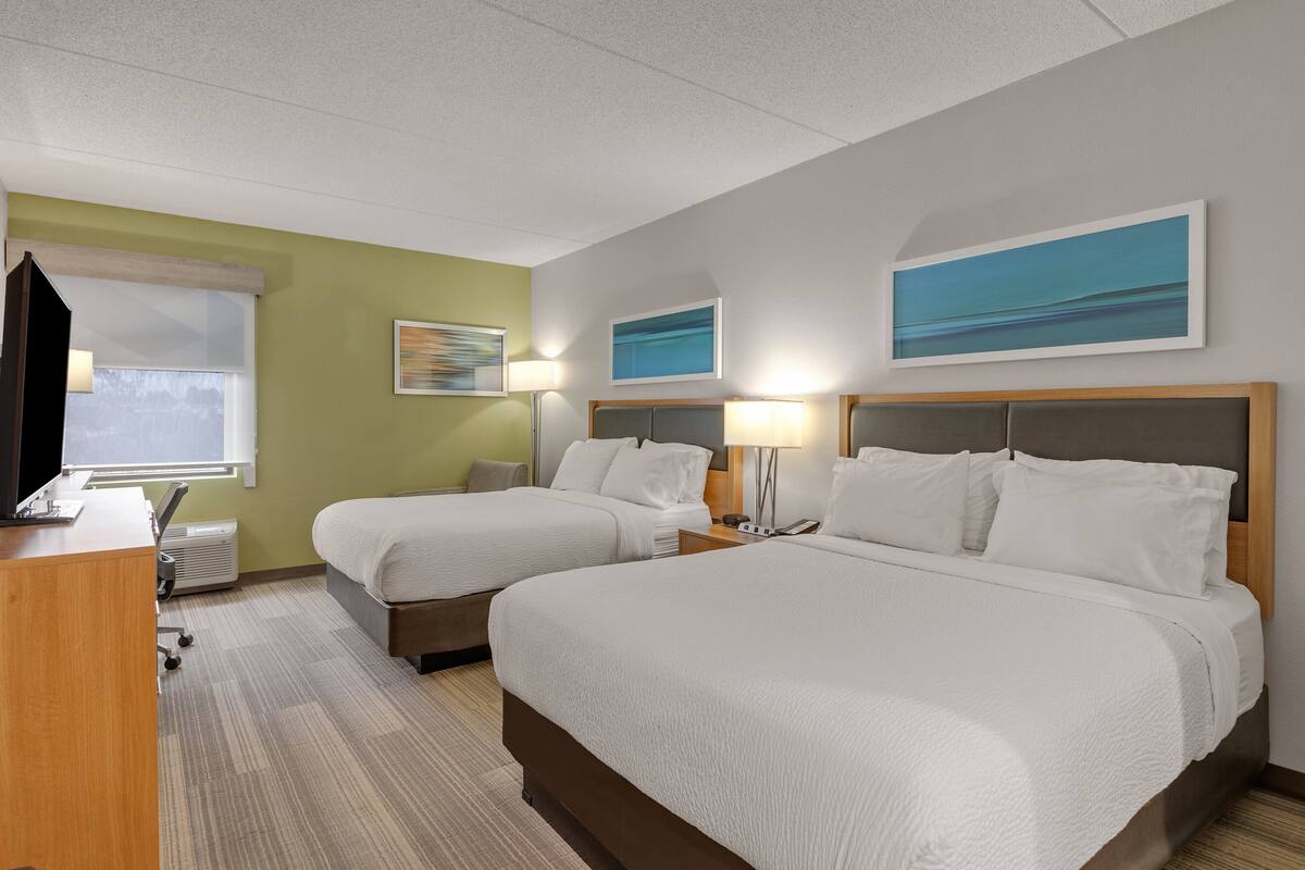 A hotel room with two beds, a desk, and a window.