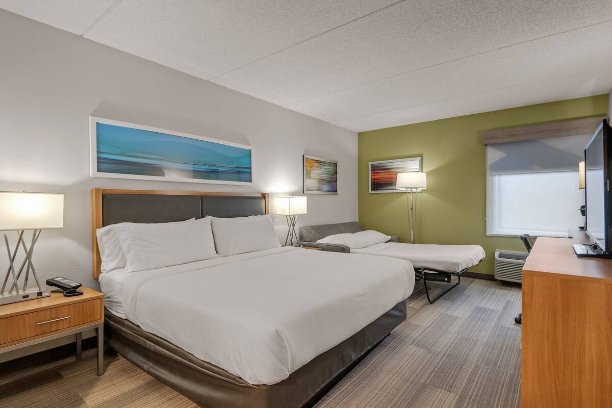 A hotel room with a large bed, a smaller bed, a desk with a computer, and a TV.