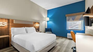 A hotel room with a bed, bedside table, lamp, desk, chair, and a window with a view.
