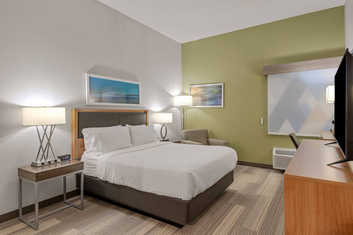 A hotel room with a bed, two bedside tables with lamps, a desk with a television, and artwork on the walls.