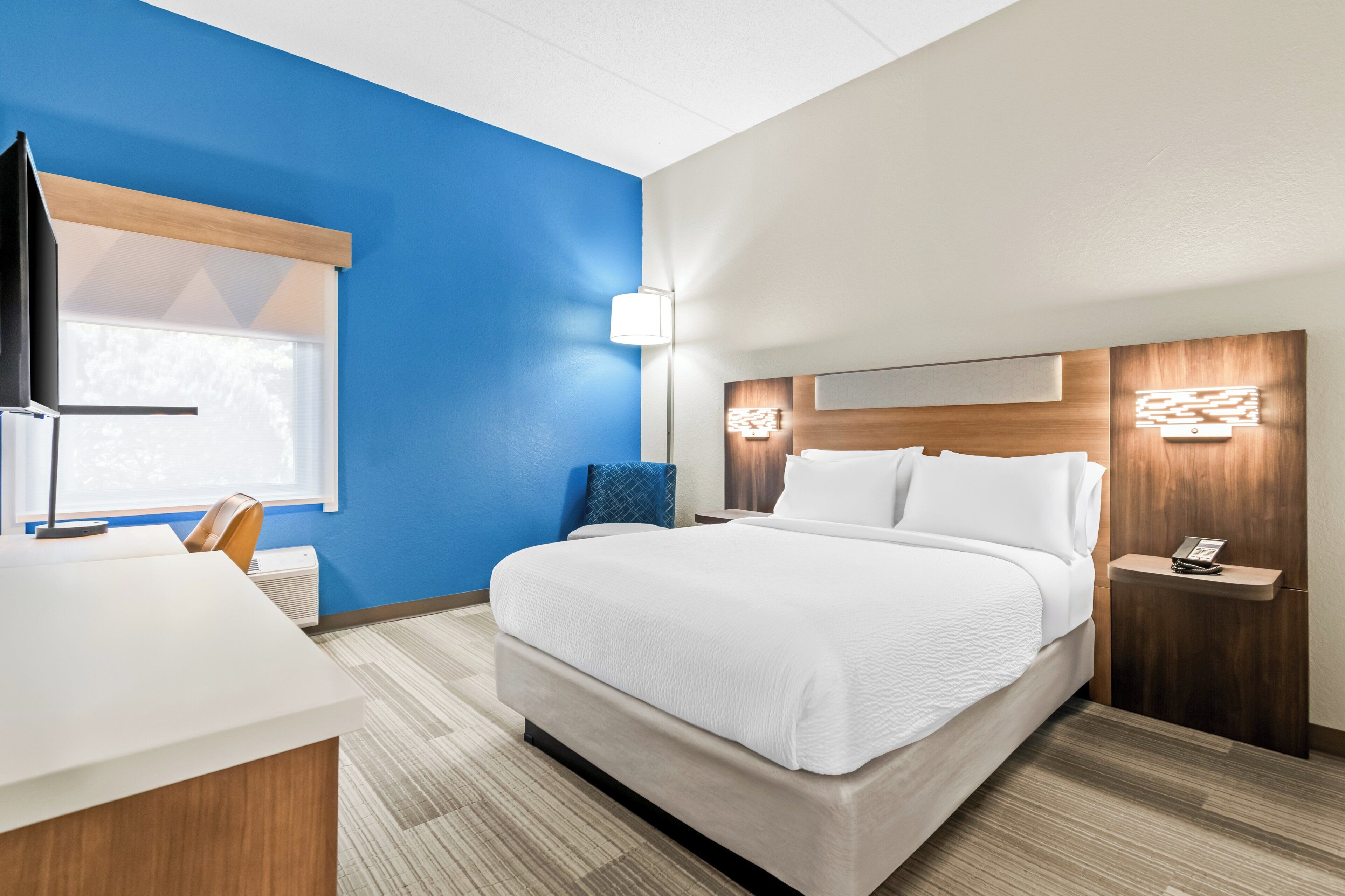 Una habitación de hotel con una cama, un escritorio, una silla, una mesita de noche y una lámpara.