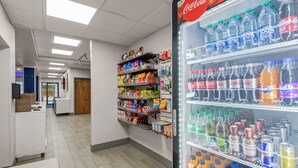 A clean, well-lit corridor with a Coca-Cola refrigerator stocked with various beverages, snack shelves, and a wooden door at the end. - Holiday Inn Express Hershey - Harrisburg Area by IHG (Hummelstown)