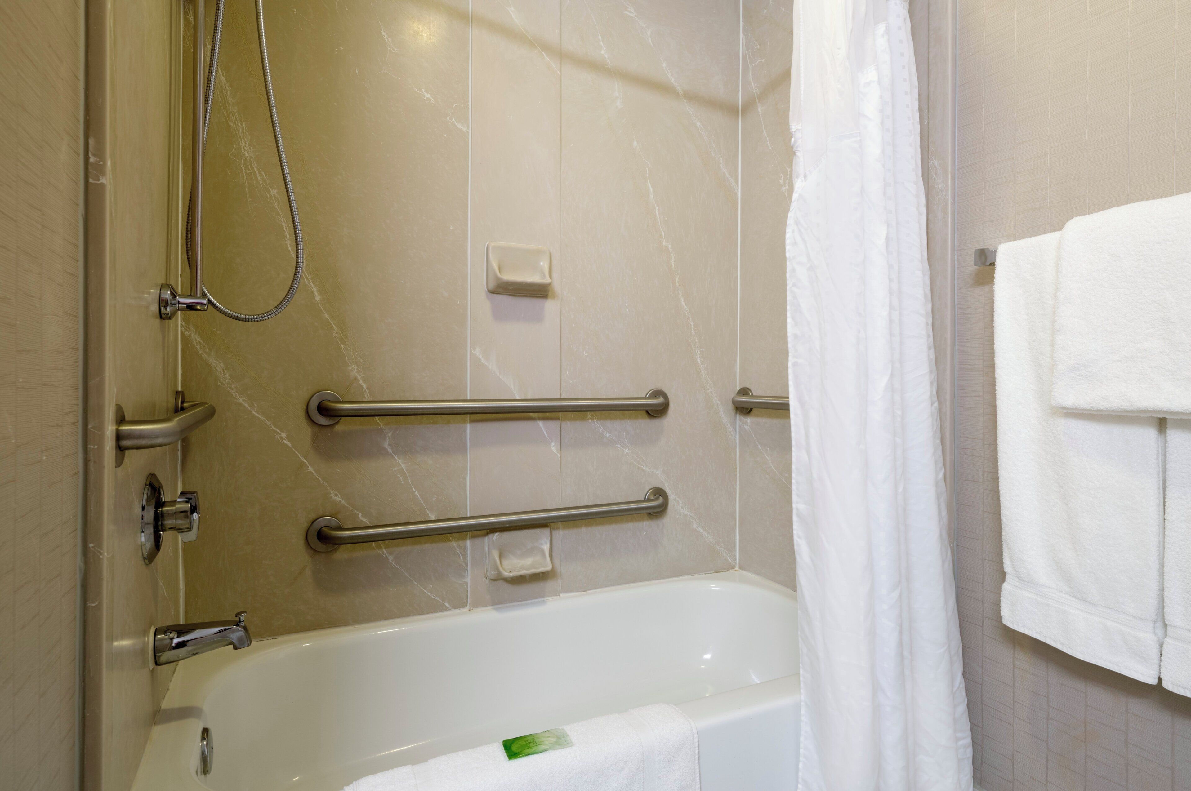 Baño con bañera, barras de apoyo, cabezal de ducha y un perchero.