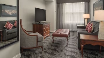 Une chambre d’hôtel moderne dotée d’un grand téléviseur à écran plat, d’un canapé gris, d’une armoire en bois et d’un tapis à motifs.