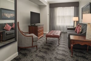 A modern hotel room with a large flat-screen TV, a grey sofa, a wooden cabinet, and a patterned carpet. - Embassy Suites by Hilton Portland Downtown (Portland)