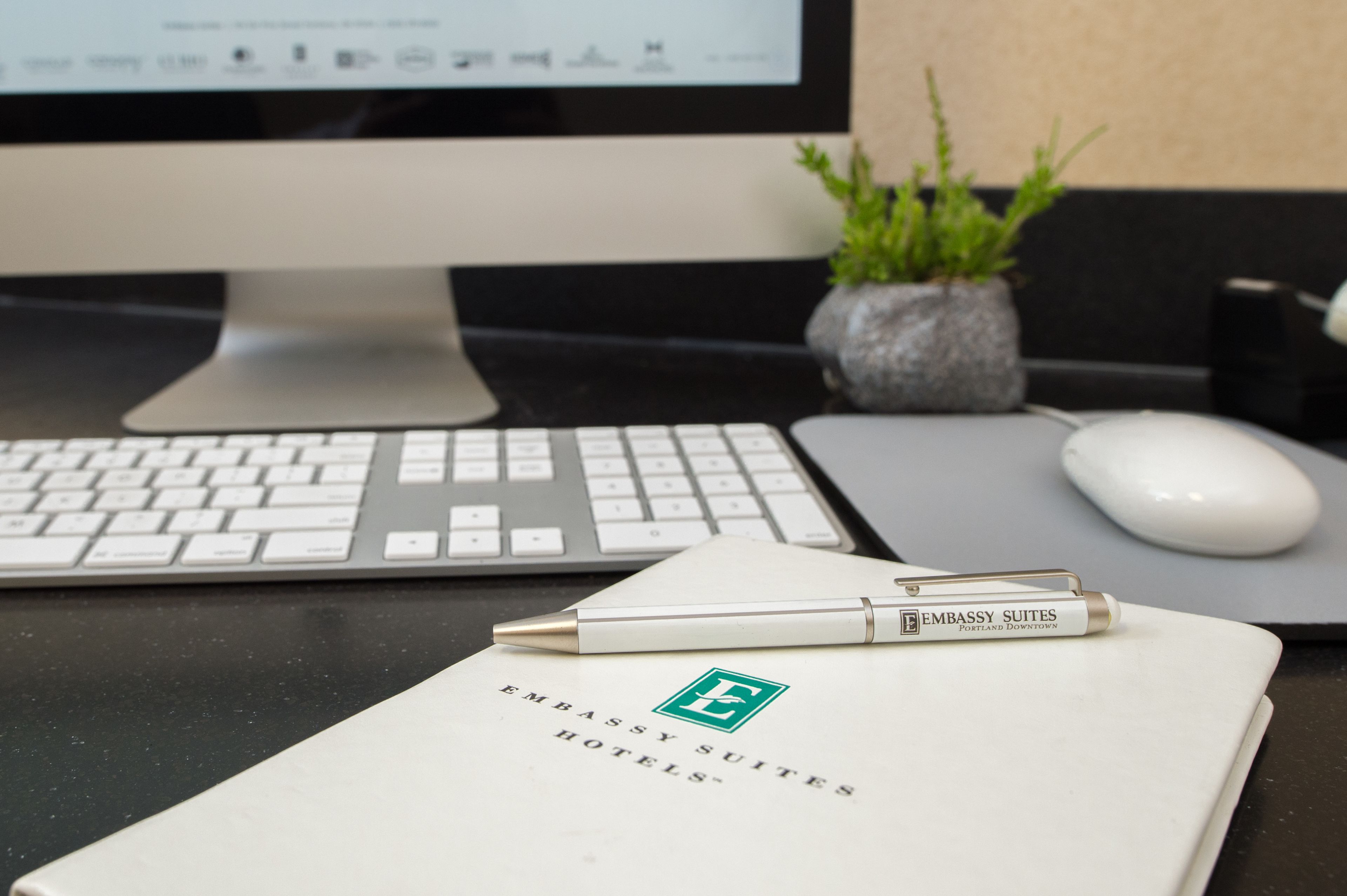 A desk with a keyboard, a mouse, a pen, and a notebook with the logo of Embassy Suites Hotels.