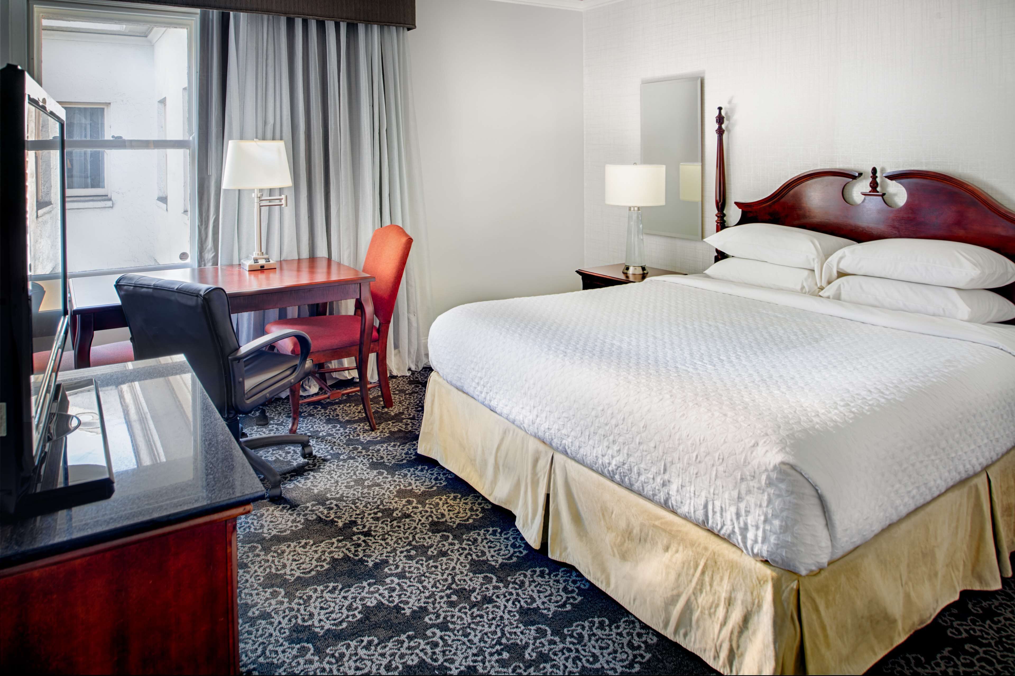 A hotel room with a bed, desk, chair, and a window with curtains.