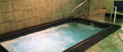 A rectangular hot tub with a black border, tiled walls, and a metal handrail.
