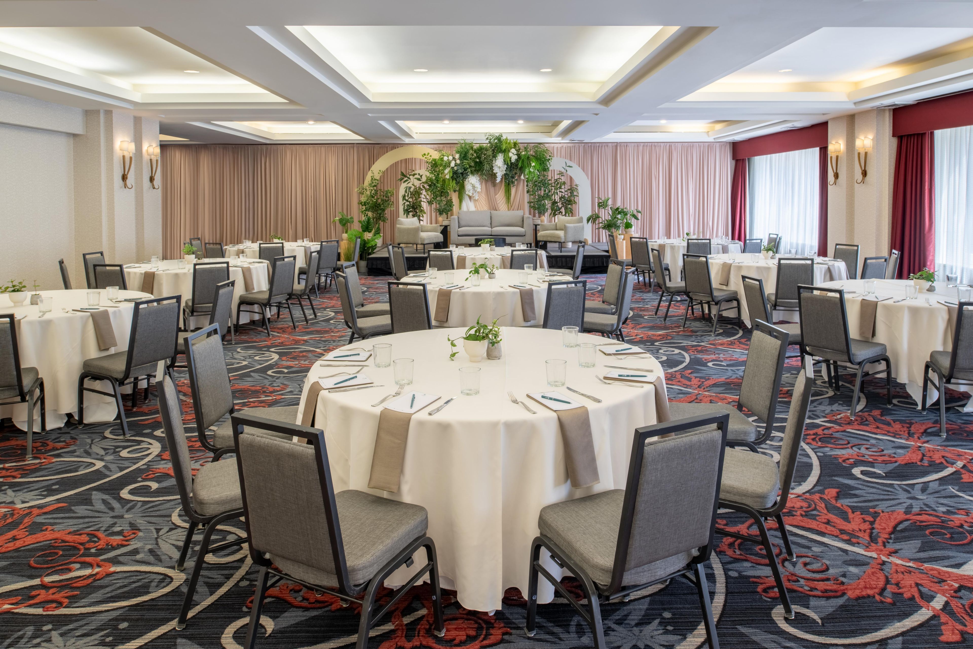 Et mødelokale med runde borde, stole og en scene.