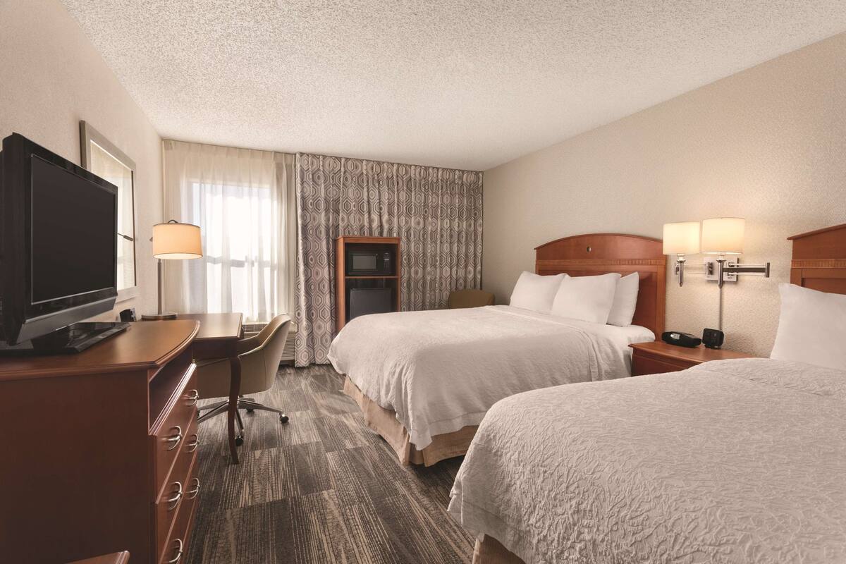 A hotel room with two beds, a desk, a television, and a microwave.