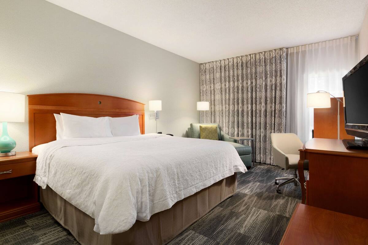 A hotel room with a large bed, a desk, a chair, and a television.